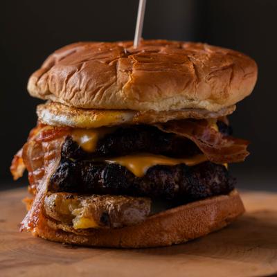 Tall burger - a fried egg, bacon, melted cheese, grilled patties between toasted buns.