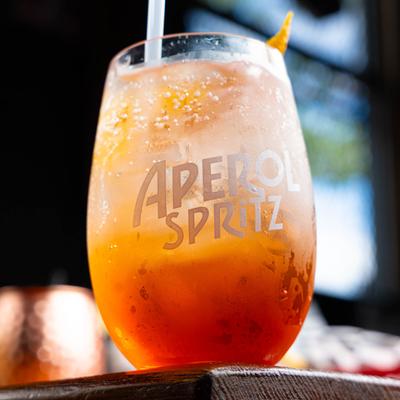 An orange Aperol Spritz cocktail with ice in a branded stemless glass.
