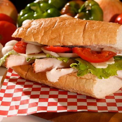 Turkey sub sandwich with lettuce, tomatoes, and provolone cheese, surrounded by fresh vegetables.