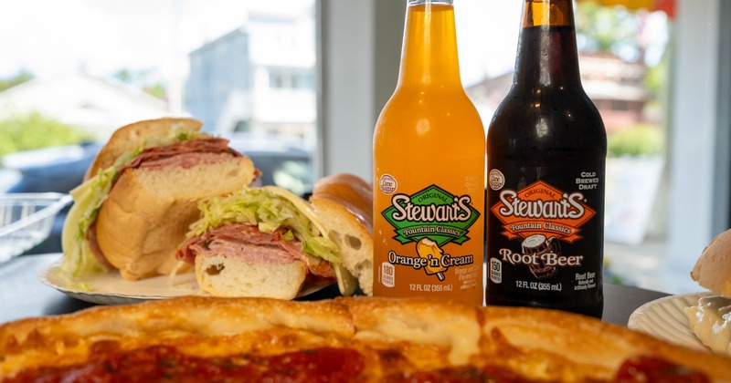 Whole pizza served alongside a sub sandwich and two bottles of soda