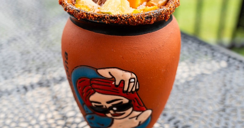 Cantarito cocktail served in a chili-rimmed clay pot with various garnsihes