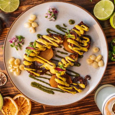Grilled octopus with yellow sauce, Peruvian corn, limes, avocado on wooden table.