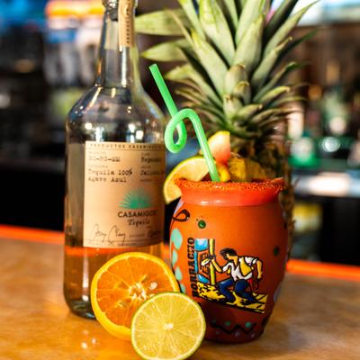 Casamigos tequila bottle beside a vibrant clay cantarito cocktail with citrus and pineapple.