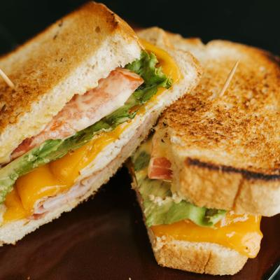 A toasted sandwich with layers of turkey, cheddar cheese, lettuce and tomato..