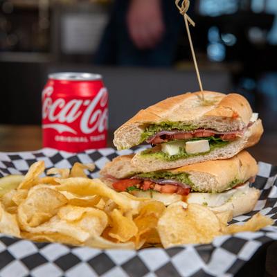 Sandwich with prosciutto, tomato, basil, balsamic, pesto, and potato chips on the side.