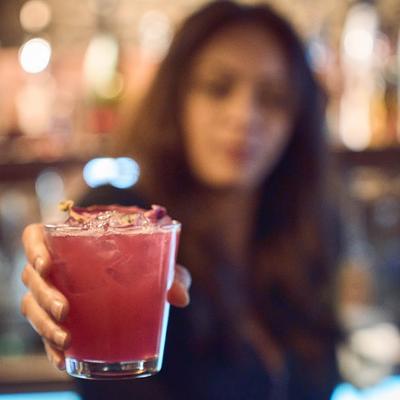 A glass of drink being held in front of the camera by a bartender.