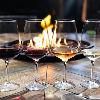 A fire pit table with lined up glasses of different types of wine.