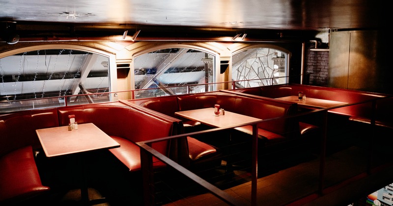 Interior view of a restaurant seating area with deep red leather booths and wooden tables