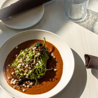 Stuffed poblano pepper served in a dark sauce, topped with crumbled cheese and herbs.