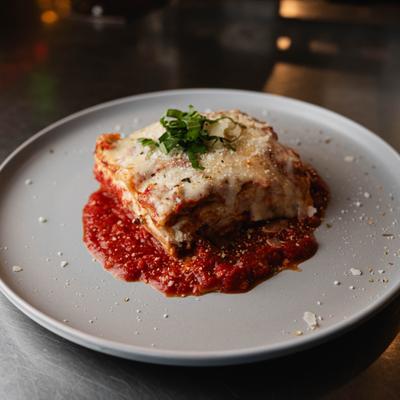 A slice of lasagna on marinara sauce topped with cheese and basil.