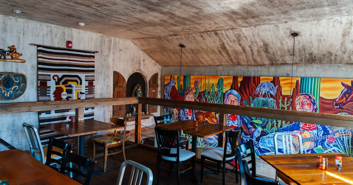 Interior of a dining area with wooden tables, mixed chairs, and a colorful mural on the wall