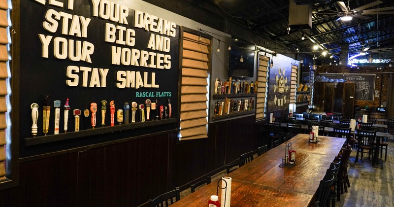 Interior of a restaurant with a long wooden table, colorful beer taps on the wall