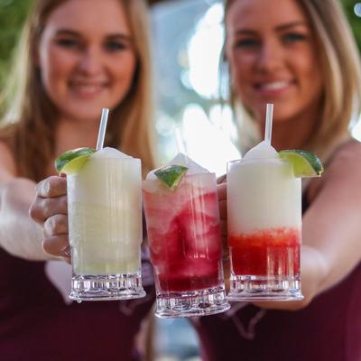 Two people holding frozen cocktails in glass mugs.