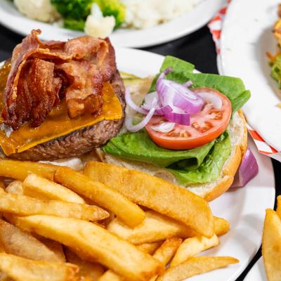 Juicy burger with bacon lettuce cheese, onions, and tomatoes with a side of fries..