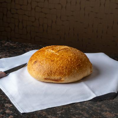 A round, golden loaf of bread sits on white cloth.