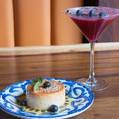 Coconut Flan garnished with blueberries and mint, alongside a cocktail.
