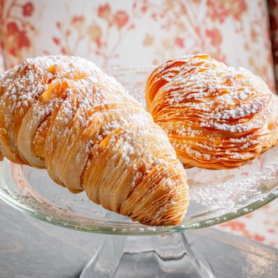 Flaky Italian pastries dusted with powdered sugar on a glass stand.