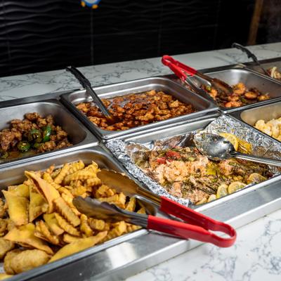 A buffet counter filled with various hot Asian dishes in metal trays.