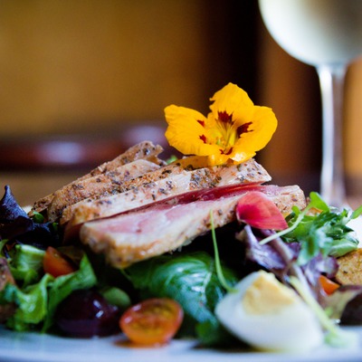 Seared tuna with mixed greens, eggs, tomatoes, and an edible flower.