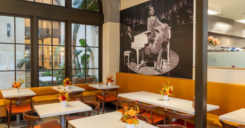 Interior of a café with white tables, orange chairs, and a large black-and-white photo on the wall