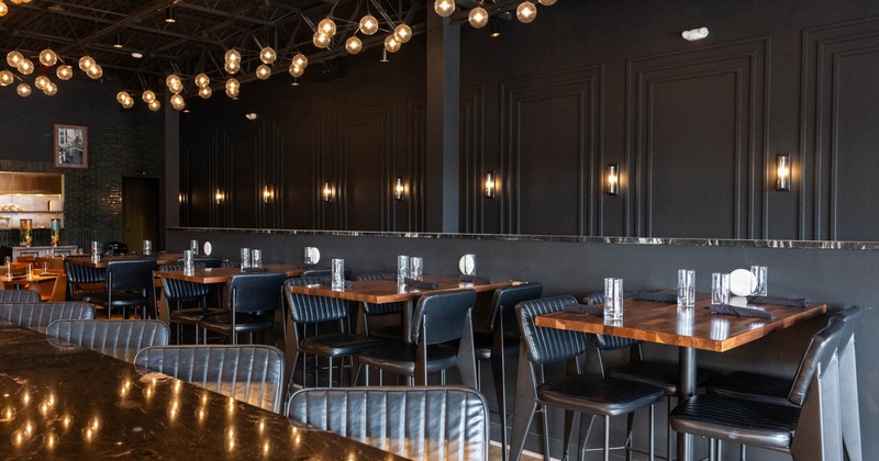 Interior with dark décor, wooden tables, black chairs, and pendant lighting