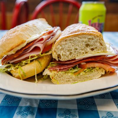 Italian sub on a white plate, sits on a blue and white checkered table.