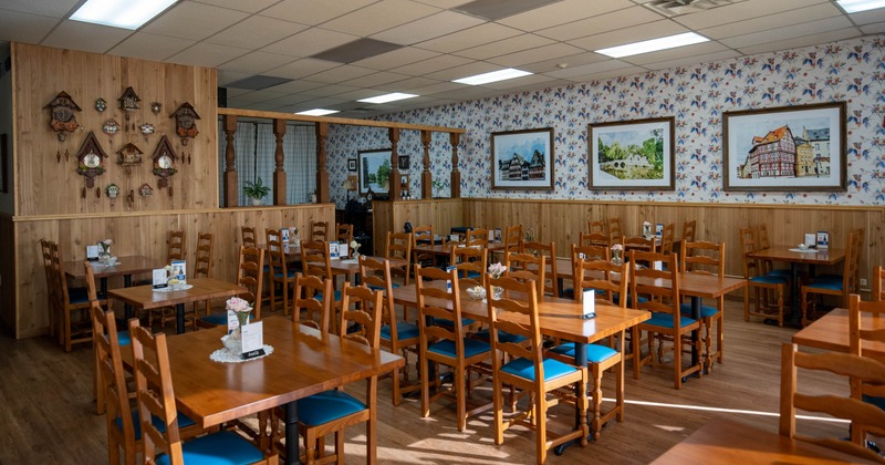 Cozy interior, wooden tables and chairs, floral wallpaper with framed paintings and cuckoo clocks