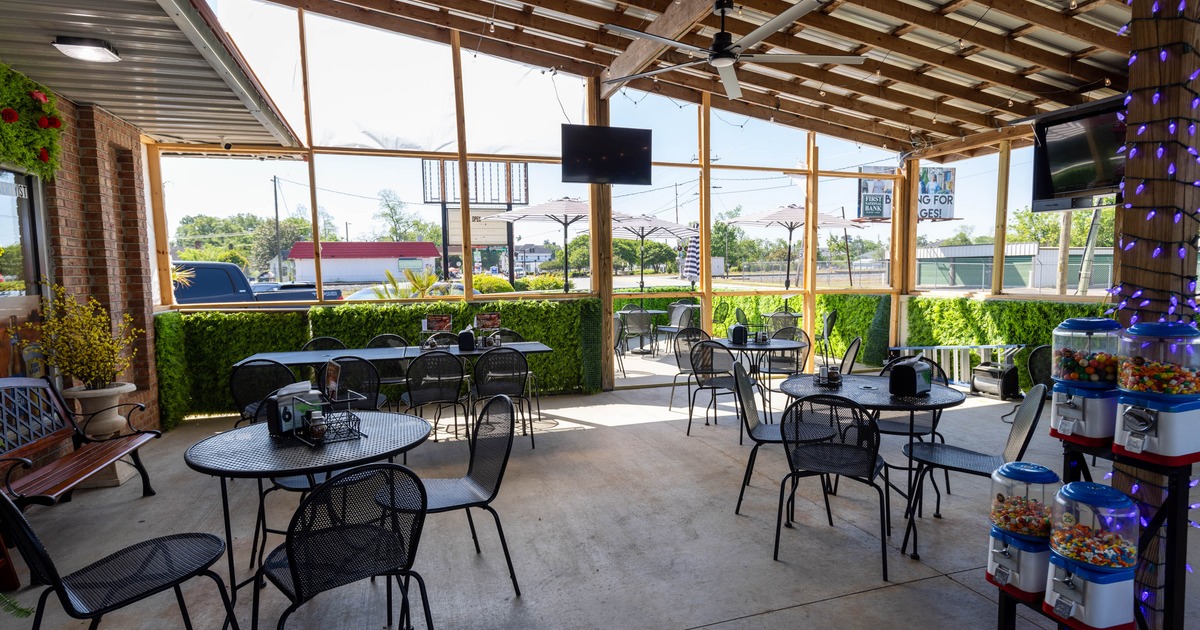 Outdoor patio - metal tables and chairs under a wooden roof with a hedge border; decorative lights