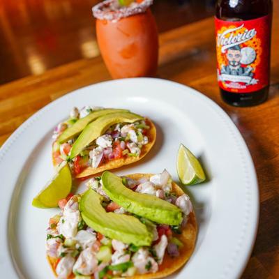 Ceviche tostadas served on a wooden table with a bottle of beer and Cantarito.