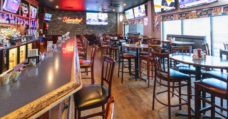 A spacious bar interior featuring a long counter, high-backed wooden chairs
