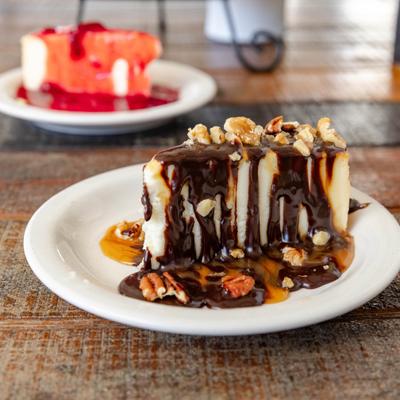 Slice of Turtle Cheesecake with Strawberry Cheesecake in the background.