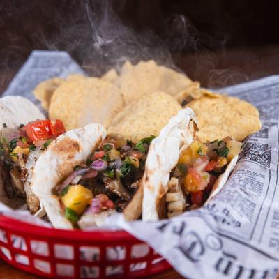 Several tacos and tortilla chips served in a red basket.