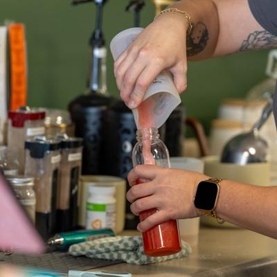 Bartednder pouring drink into a plastic bottle.