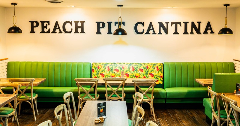 Inside, seating area with green booths, wooden tables, and chairs under pendant lights