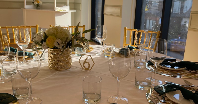 Table setup for an event, featuring gold chairs, glassware, and a floral centerpiece