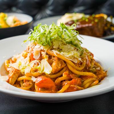 A plate of thick pasta with tomato sauce, garnished with shredded lettuce and Parmesan cheese.