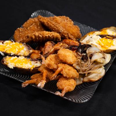 A plate of fried shrimp, chicken tenders, twice-baked potatoes, and grilled onions.