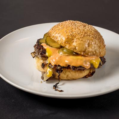 Oklahoma Fried Onion Burger topped with sauce and sliced pickles.