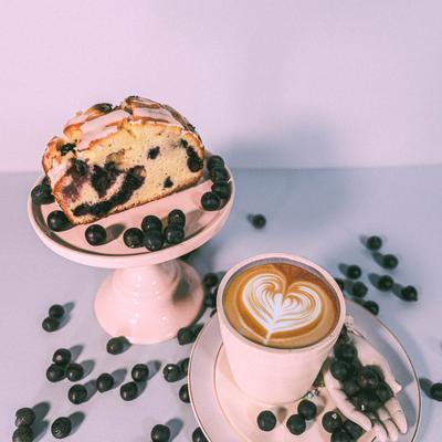 Blueberry loaf cake with icing served with a latte and scattered blueberries.