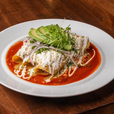 Flautas in red sauce, topped with cheese, sour cream, and avocado.