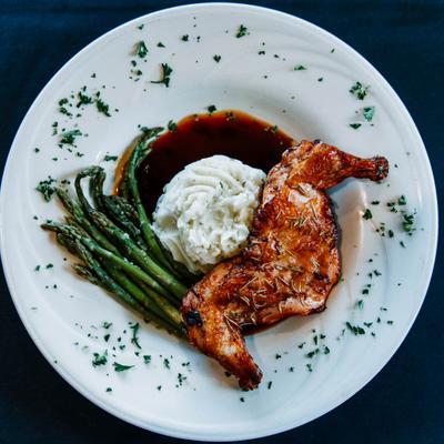 Roasted chicken served alongside mashed potatoes, asparagus, and rosemary demi-glace.