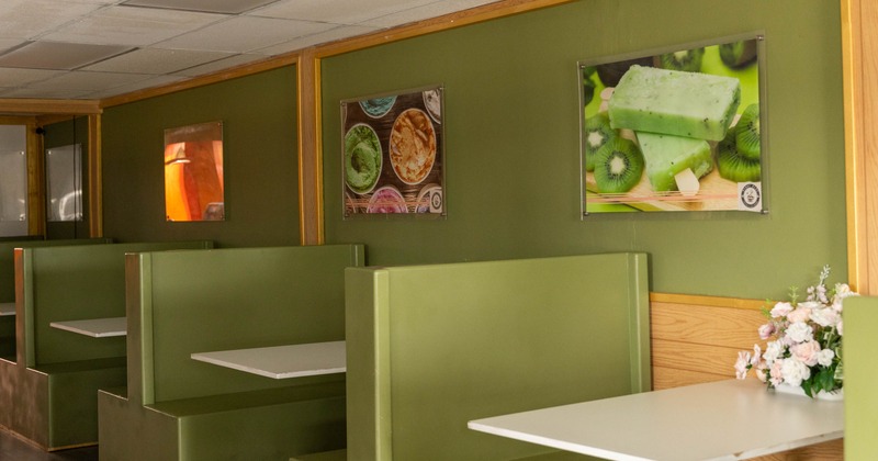 Interior of a café with olive-green booths and framed food photos on a green wall