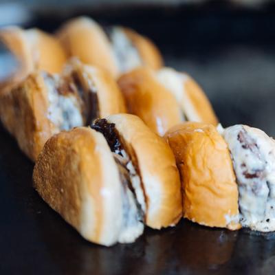 Mini sandwich sliders with creamy filling and meat arranged in a row.
