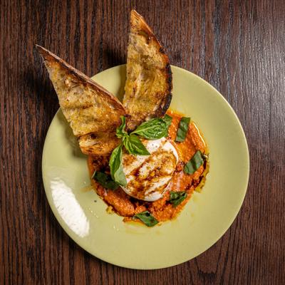 Burrata served with grilled bread on a green plate atop a wooden table.