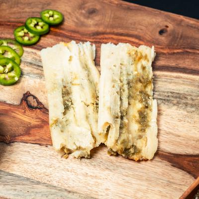 Tamales on a wooden board with sliced green pepper, top view.