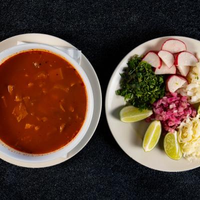 Menudo soup served alongside a plate with sides and condiments.