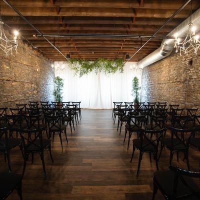 Industrial wedding venue with brick walls, wooden floors, and chairs.