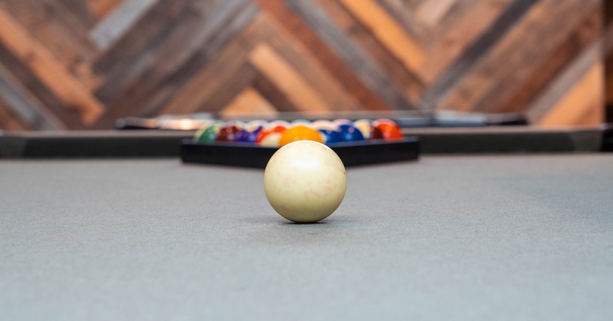 Close-up of a cue ball on a pool table with a rack of colorful balls in the background