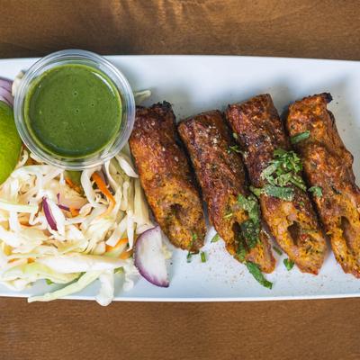 Grilled seekh kebabs with cabbage slaw and green chutney on a white plate.