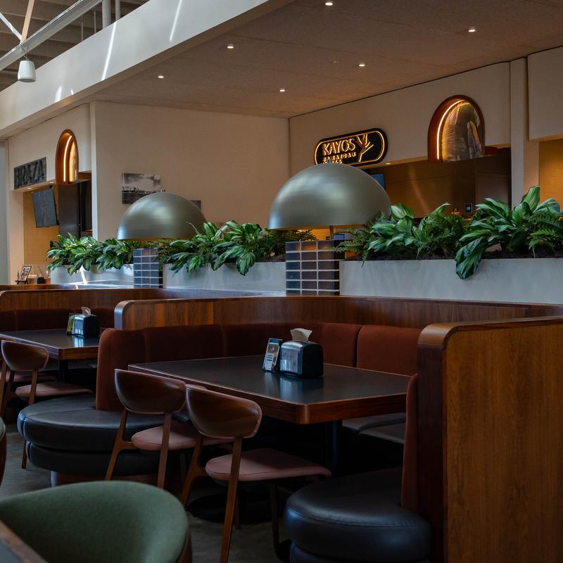 Modern dining area with wooden booths, green plants, and overhead lighting